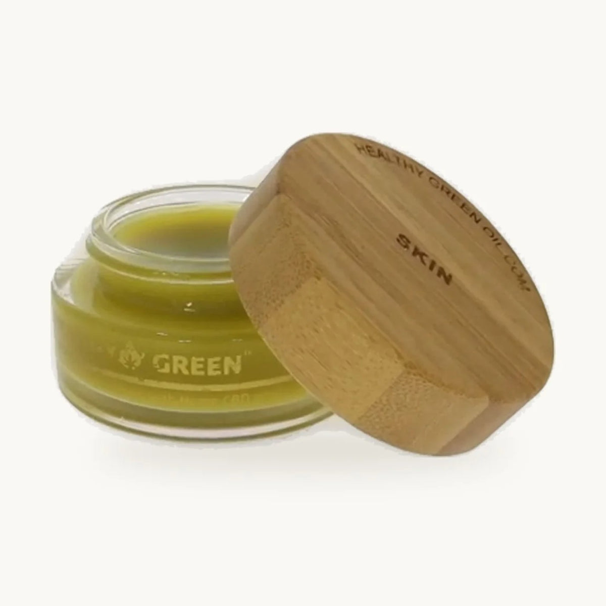 Healthy Green Botanical Balm — Skin, open glass jar of pale green balm with its engraved bamboo lid, on a soft cream background