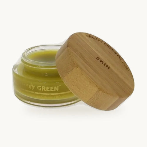 Healthy Green Botanical Balm — Skin, open glass jar of pale green balm with its engraved bamboo lid, on a soft cream background